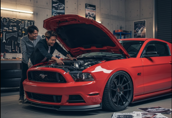 ガレージの中でカスタムされたマスタング5代目を囲み、楽しそうに話している日本人男性2人。ホイールやエアロパーツが交換されており、個性的な雰囲気を醸し出している。